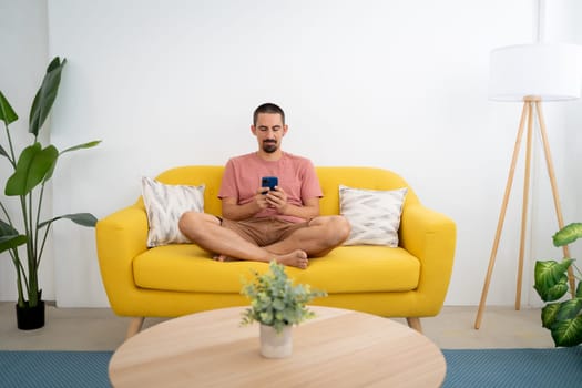 Smiling young man with smartphone sitting on sofa at home. High quality photo