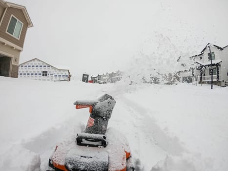 Denver, Colorado, USA-February 4, 2024-View from a snow-blanketed driveway captures a residential area mid-snowfall, with houses partially obscured by the cascading white flakes and a snow-covered car in the foreground.