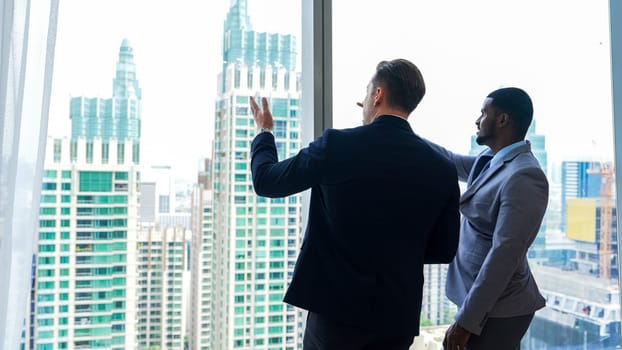 Back view diverse team of ambitious business people standing in ornamented office gazing out window to cityscape skyline. Determination and business ambition drive their career toward to bright future