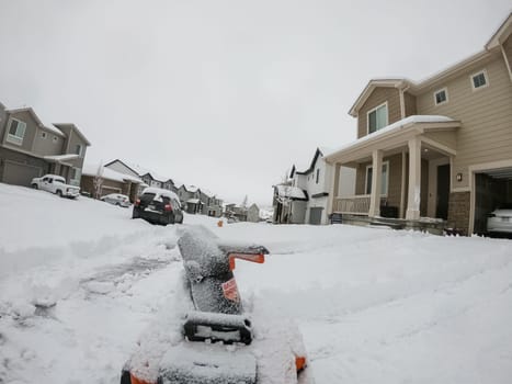 Denver, Colorado, USA-February 4, 2024-View from a snow-blanketed driveway captures a residential area mid-snowfall, with houses partially obscured by the cascading white flakes and a snow-covered car in the foreground.