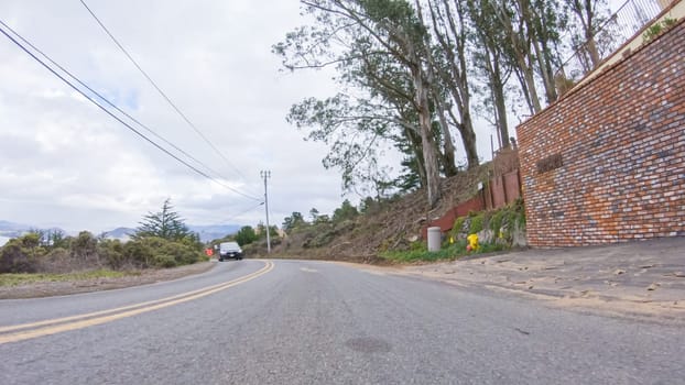 Vehicle navigates the streets of Morro Bay, California, during a cloudy winter day. The atmosphere is moody and serene as the overcast sky casts a soft light on the charming buildings and quiet streets of this coastal town.