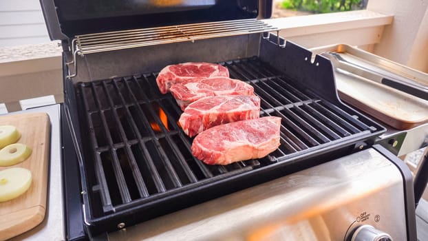 The outdoor two-burner gas grill is put to good use, sizzling with the sound and aroma of ribeye steaks and onion rings being perfectly cooked.