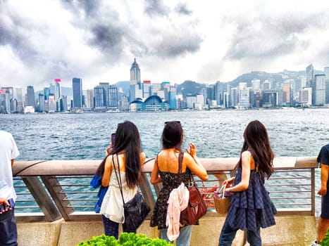 Hong Kong - April 05, 2024: People gather on the Hong Kong waterfront, with skyscrapers and Victoria Bay in the background on a cloudy afternoon