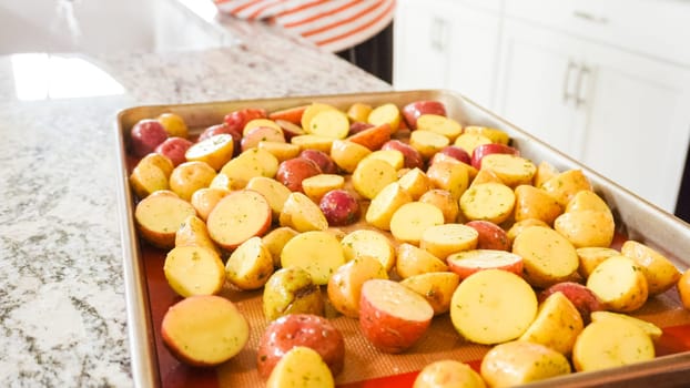 In a modern, white kitchen, a young man is engrossed in dinner preparations. His current endeavor includes arranging seasoned rainbow potatoes on a baking sheet, a meticulous step towards a promisingly tasty meal.