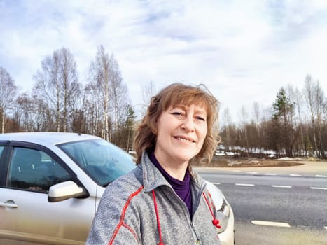 A woman takes a selfie on the road near a car. The concept of car travel. A woman captures a selfie with her car in the background during road trip