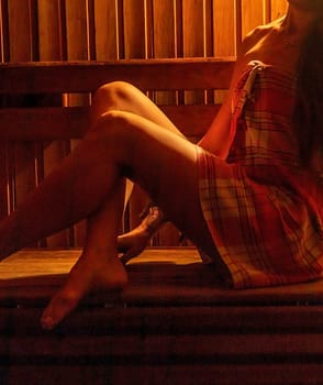 Shot of the woman with beautiful body, wrapped in checkered towel in the dark, warm sauna room