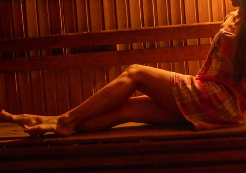 Shot of the woman with beautiful body, wrapped in checkered towel in the dark, warm sauna room