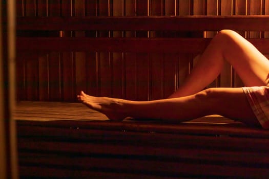 Shot of the woman with beautiful body, wrapped in checkered towel in the dark, warm sauna room