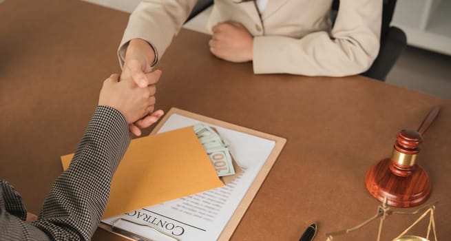 Close-up of business handshake with money in envelope on desk. Concept of business agreement and financial transaction.