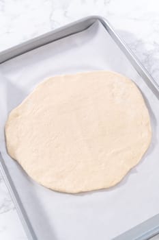 Preparing cinnamon dessert pizza on a baking sheet lined with parchment paper.