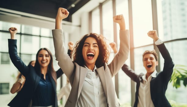 Happy overjoyed laughing woman employee celebrating success raising her hands up with group of colleagues having fun in the office