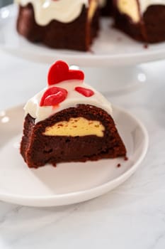 Slicing freshly baked red velvet bundt cake with chocolate lips and hearts over cream cheese glaze for Valentine's Day.