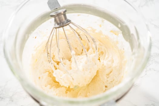 Mixing ingredients in a large glass mixing bowl of kitchen mixer to make eggnog buttercream frosting.