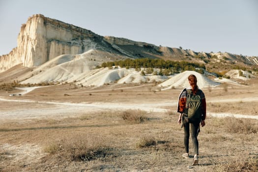 adventurer standing in field with backpack and mountain backdrop