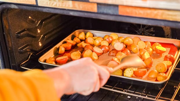 Within the setting of a modern kitchen, a young man is immersed in preparing dinner, currently roasting seasoned rainbow potatoes in the oven, an important step towards a delightful meal.