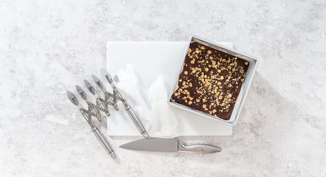 Flat lay. Removing chocolate hazelnut fudge from a square cheesecake pan lined with parchment.