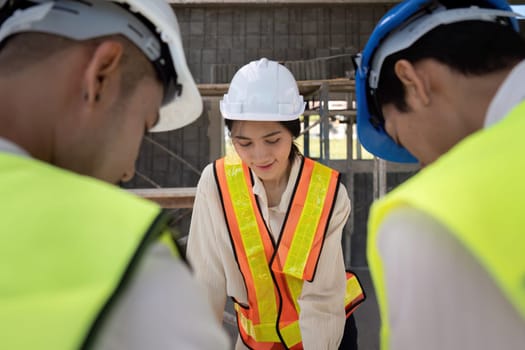 Asian female engineer with colleagues discussing construction plans, teamwork on-site.