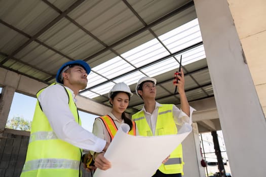 Asian female engineer with colleagues reviewing blueprints at construction site, teamwork concept.