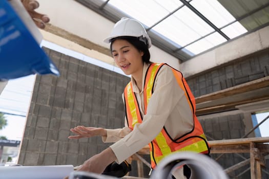 Asian female engineer reviewing construction plans on-site, project management concept.