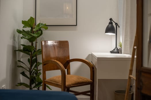 A cozy minimalist home office featuring a wooden chair, desk lamp, houseplant, and white desk, creating a tranquil workspace environment.