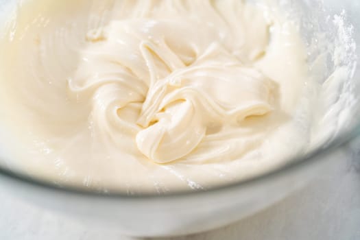 Mixing ingredients in a large glass mixing bowl to make the cream cheese glaze.