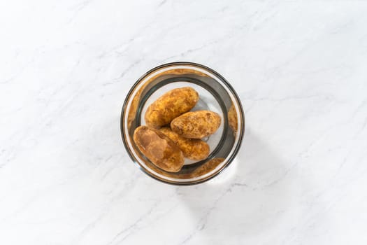 Flat lay. Pressure Cooker Baked Potatoes. Washing raw potatoes in a glass mixing bowl with water.