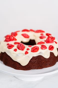 Freshly baked red velvet bundt cake with chocolate lips and hearts over cream cheese glaze for Valentine's Day.