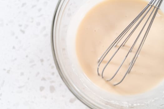 Mixing ingredients with a hand whisk in a glass mixing bowl to make the vanilla glaze.