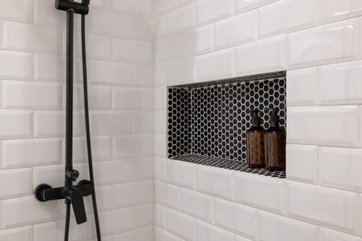 Elegant white tiled shower with black fixtures, featuring a built-in shelf with stylish black tiles and brown soap bottles. Perfect for contemporary bathroom designs.