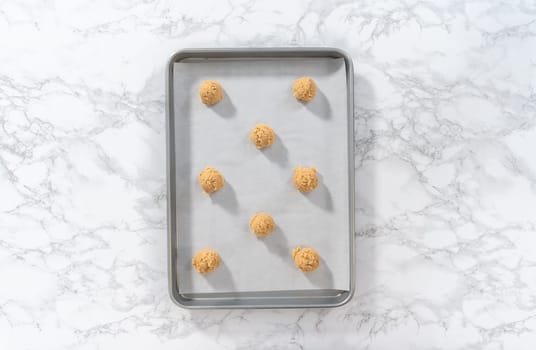 Flat lay. Scooping cookie dough with dough scoop into a baking sheet lined with parchment paper to bake eggnog cookies with a chocolate gingerbread man.
