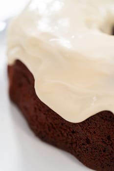 Pouring cream cheese glaze over freshly baked red velvet bundt cake.