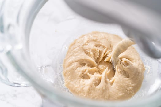 Mixing ingredients in a large glass mixing bowl to pizza dough.