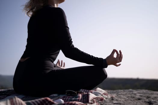 A woman is sitting on a rock with her hands on her knees. She is wearing black clothing and a scarf. Concept of calm and relaxation, as the woman is practicing yoga or meditation