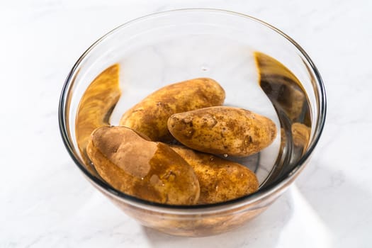 Pressure Cooker Baked Potatoes. Washing raw potatoes in a glass mixing bowl with water.