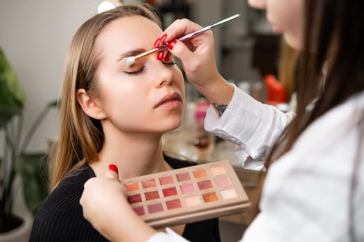 Skilled woman softly blends outer edges of eyeshadow. Professional artist ensures look uniquely suited to lady client personal style