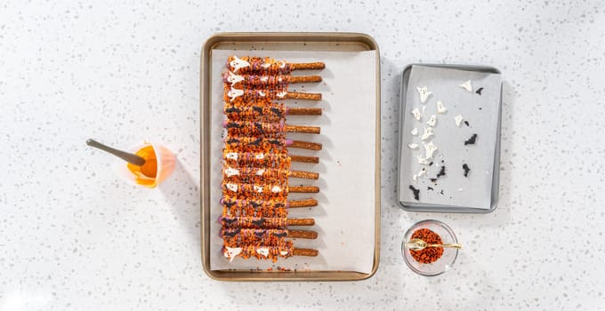 Flat lay. Dipping pretzel rods into melted chocolate to make Halloween chocolate-covered pretzel rods.