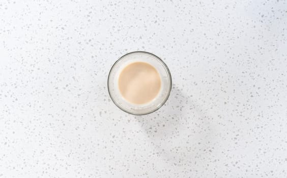 Flat lay. Mixing ingredients with a hand whisk in a glass mixing bowl to make the vanilla glaze.