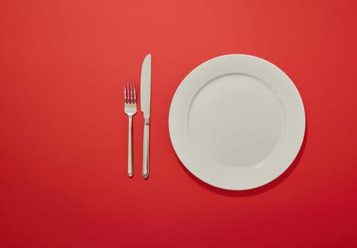 Elegant table setting with silver cutlery on red background, top view for restaurant menu or event catering concept