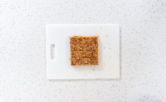 Flat lay. Cutting pumpkin spice fudge into square pieces on a white cutting board.