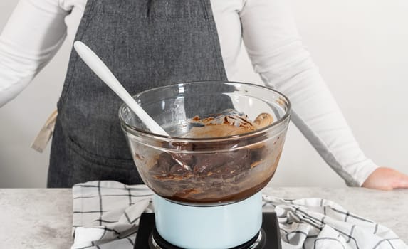 Melting white chocolate chips and other ingredients in a glass mixing bowl over boiling water to prepare chocolate macadamia fudge.