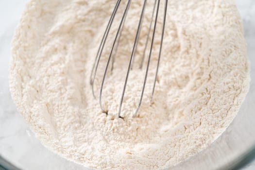 Mixing dry ingredients with a hand whisk in a large glass mixing bowl to bake American flag mini cupcakes.