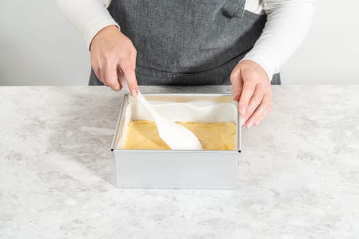 Filling square cheesecake pan lined with parchment paper with fudge mixture to prepare candy cane fudge.