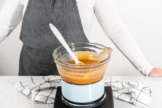 Melting chocolate chips and other ingredients in a glass mixing bowl over boiling water to prepare pumpkin spice fudge.