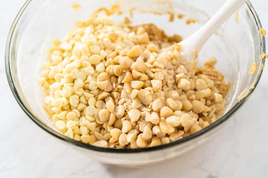 Mixing wet and dry ingredients with a hand whisk in a glass mixing bowl to bake white chocolate macadamia nut.