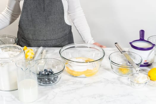 Integrating ingredients in a glass bowl, adeptly stirring with a whisk to craft a tantalizing lemon-blueberry bundt cake.