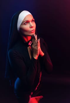 Sexy nun girl in a dress prays in the dark in neon light