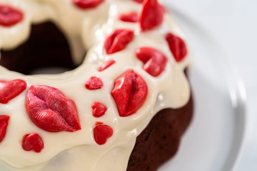 Freshly baked red velvet bundt cake with chocolate lips and hearts over cream cheese glaze for Valentine's Day.