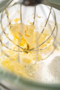 Mixing ingredients in a large glass mixing bowl of kitchen mixer to make eggnog buttercream frosting.