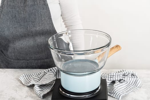 Melting chocolate chips and other ingredients in a glass mixing bowl over boiling water to prepare chocolate hazelnut fudge.