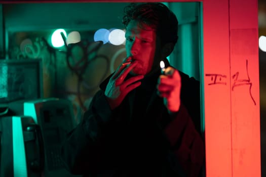 A man is smoking a cigarette in a telephone booth. The room is filled with a red and green glow, giving it a mysterious and eerie atmosphere. The man's face is obscured by the smoke